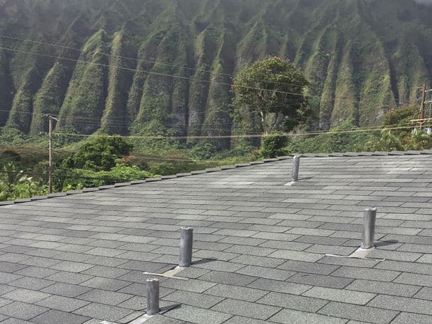 Roof covered with shingles overlooking green mountainous landscape and a clear sky.