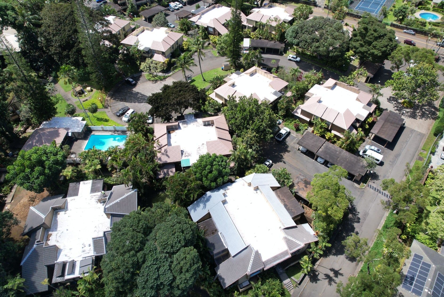Aerial view of residential neighborhood with houses, swimming pools, and lush greenery.